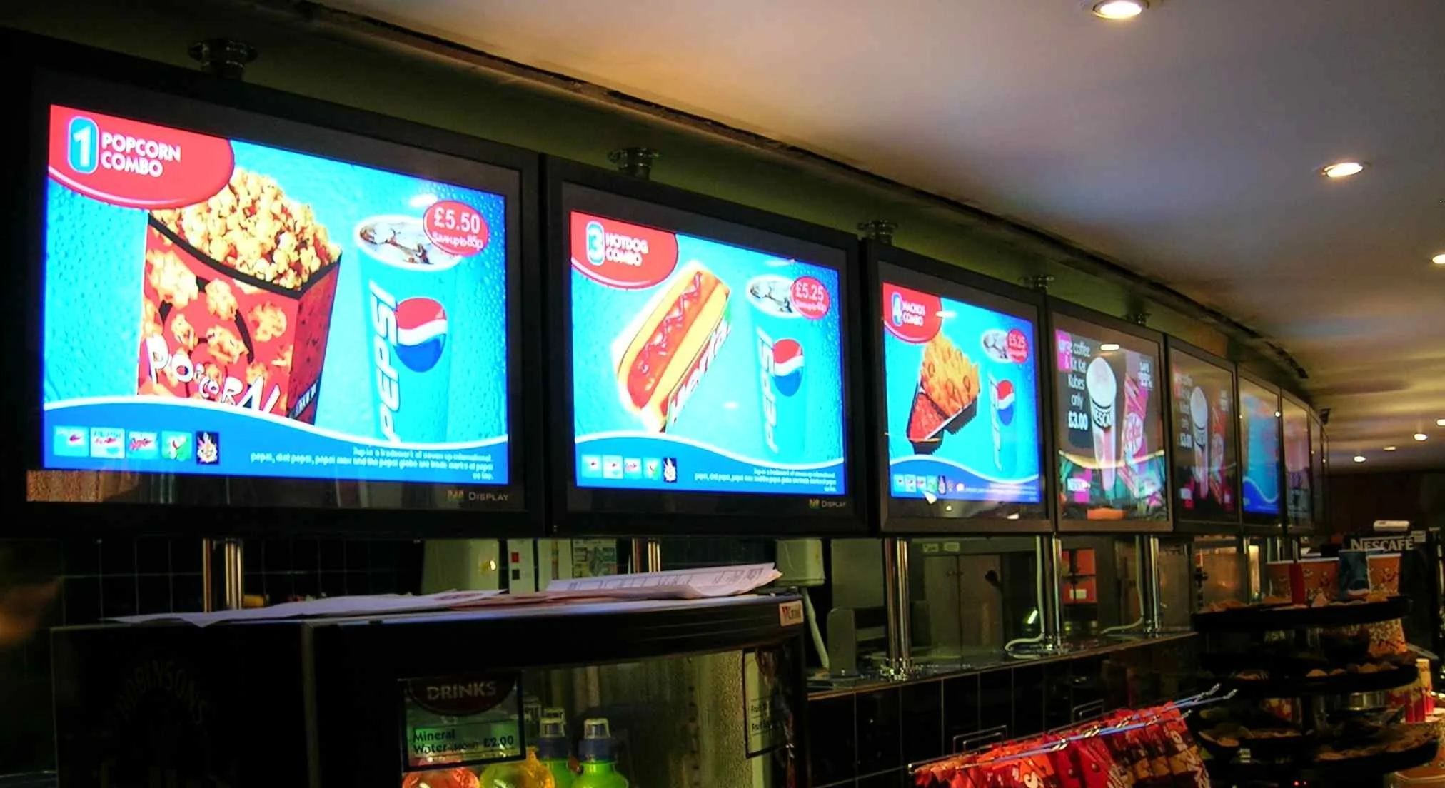 Row of digital signage menu screens at cinema concession food counter