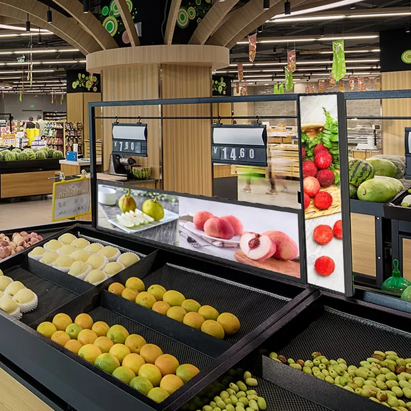 Digital signage screens installed above fresh fruit shelf in supermarket showing product pictures and prices