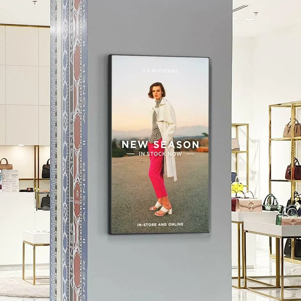 Vertical wall-mounted LCD digital display inside luxury boutique showing new season fashion campaign