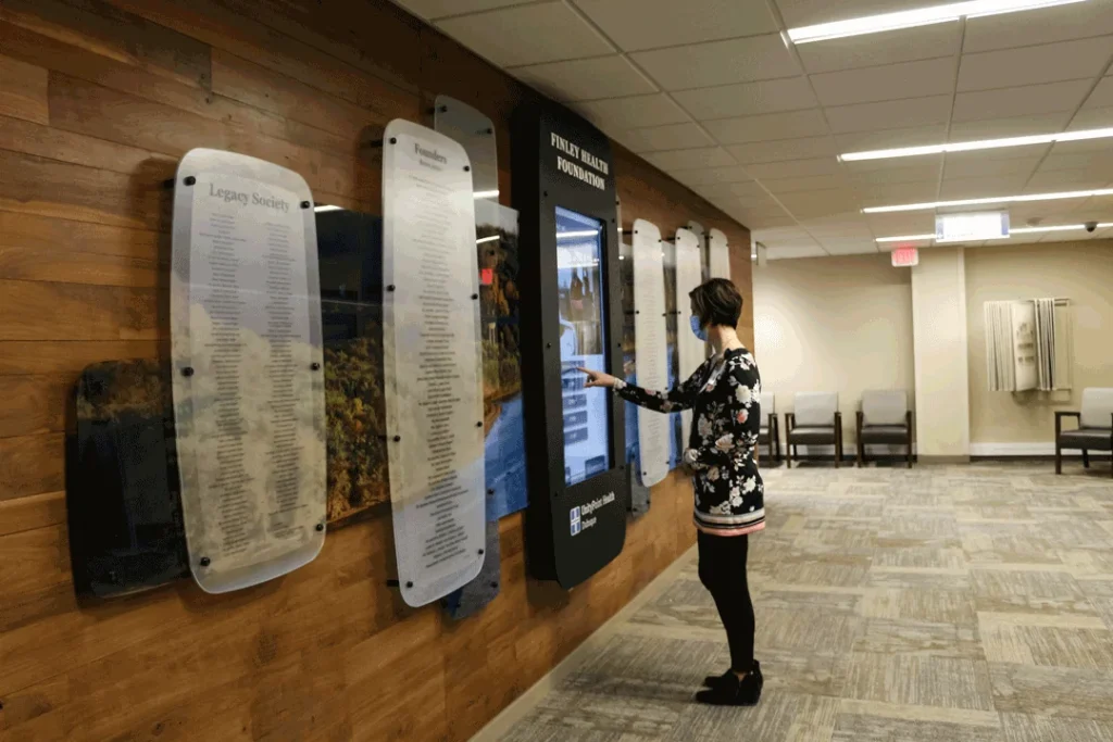 Woman touching interactive digital signage kiosk in hospital lobby