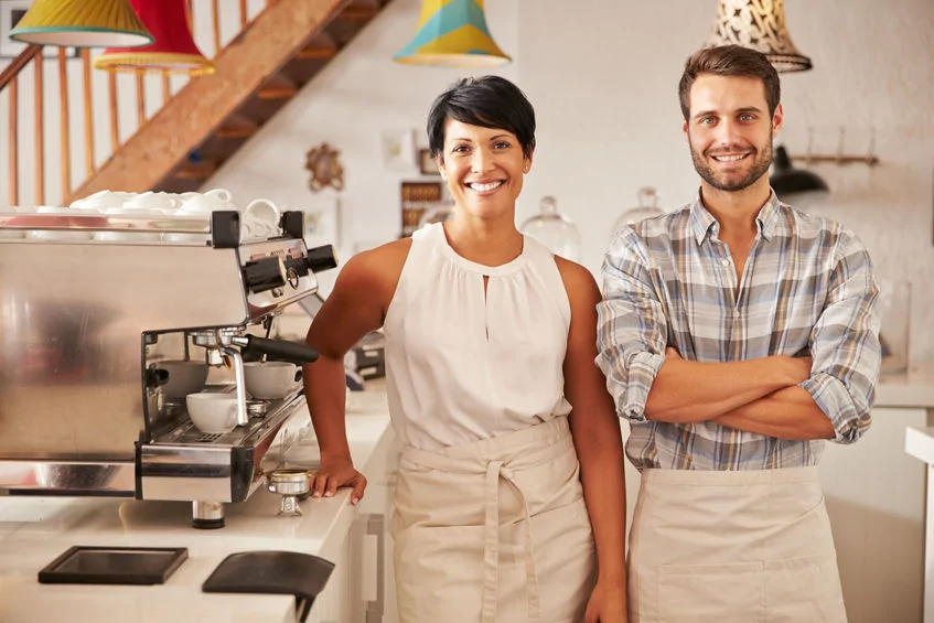 Two small business cafe owners standing behind coffee counter, small local business using digital signage for marketing