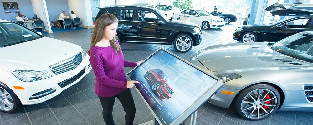 Woman using touch screen digital signage kiosk in car dealership showroom